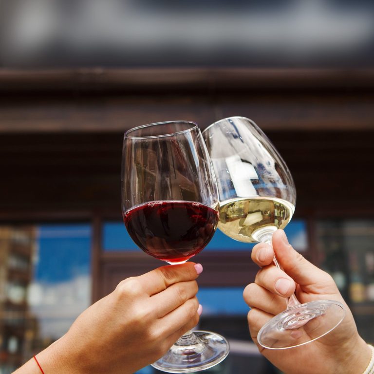 Weiß und Rot Es wird angestoßen mit zwei Weingläsern. In einem Glas befindet sich Weißwein, im anderen Rotwein.